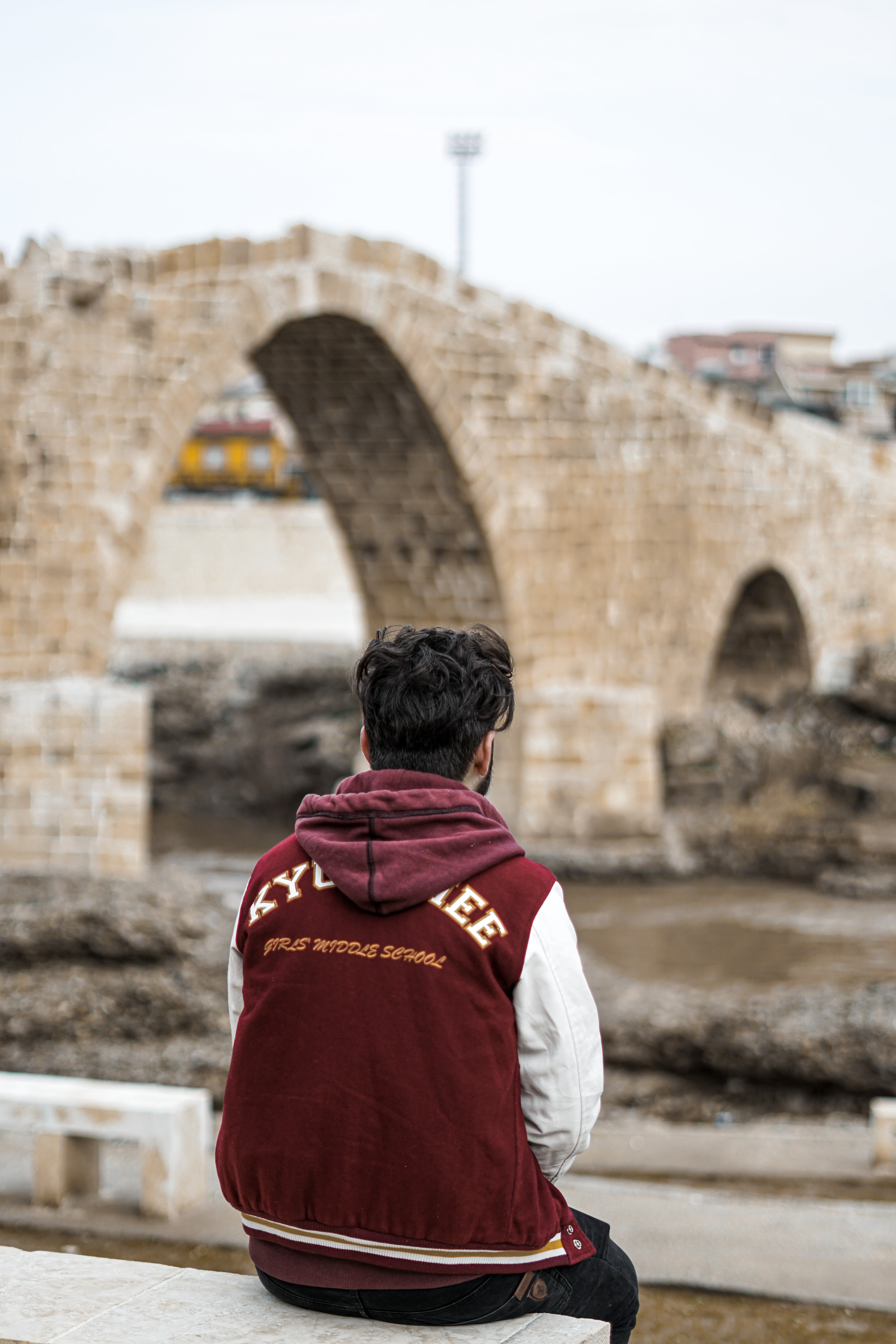 man in red hoodie standing near brown concrete bridge during daytime